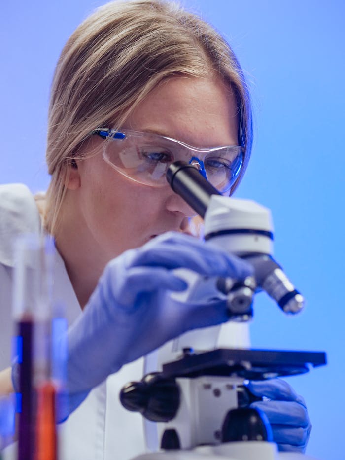 pexels photo 8325955 A female scientist wearing goggles and gloves examines a microscope slide in a laboratory.